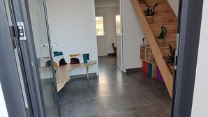 Ein modernes Interieur mit Glastür zu einem Wohnbereich, einer Holztreppe und einem Flur mit Sitzbank und Topfpflanzen.
