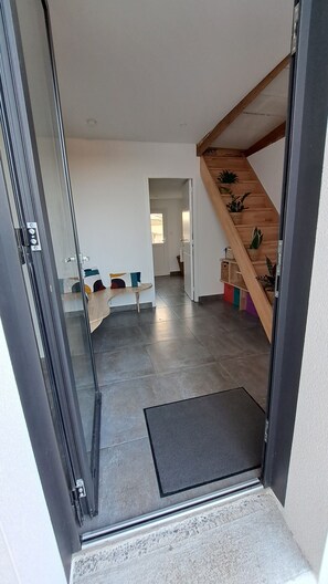 Ein modernes Interieur mit Glastür zu einem Wohnbereich, einer Holztreppe und einem Flur mit Sitzbank und Topfpflanzen.