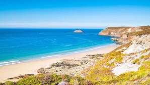 Eine Küstenlandschaft mit Sandstrand, felsigen Klippen und einer kleinen Insel in der Ferne.