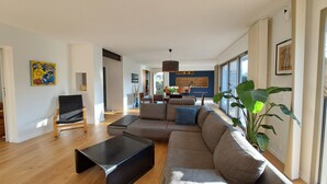 Ein modernes Wohnzimmer mit einem Ecksofa, einem schwarzen Couchtisch und einem Essbereich mit Holztisch und Stühlen.