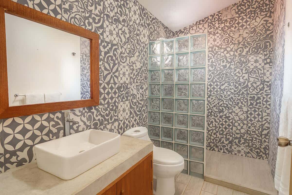 A bathroom with patterned walls, a white sink, a mirror, and a glass shower enclosure.