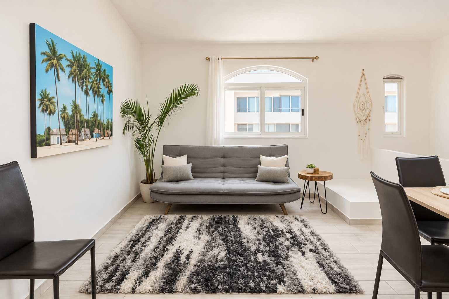 Una sala de estar moderna con un sofá gris, un tapiz blanco y negro, una mesa de comedor con sillas, una planta y un cuadro de palmeras.