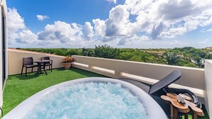 Eine Dachterrasse mit Whirlpool, Gartenmöbeln und Blick auf die Landschaft.
