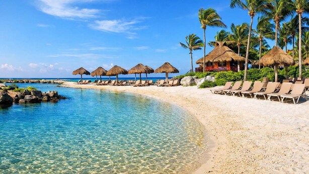 A beach resort with clear turquoise water, thatched-roof umbrellas, and palm trees. - Pool + Jacuzzi Villa • Walk to Beach • Sleeps 16 (Puerto Aventuras)