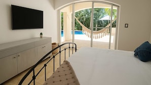 A bedroom with a bed, a TV mounted on the wall, a view of a pool and hammock outside. - Pool + Jacuzzi Villa • Walk to Beach • Sleeps 16 (Puerto Aventuras)