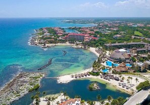 An aerial view of a coastal resort with a marina, beachfront, and multiple buildings with red roofs. - Townhouse | Garden + BBQ | 5-min to Beach | Pool (Puerto Aventuras)