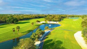 Campo de golfe com lago, bunkers de areia e céu limpo.