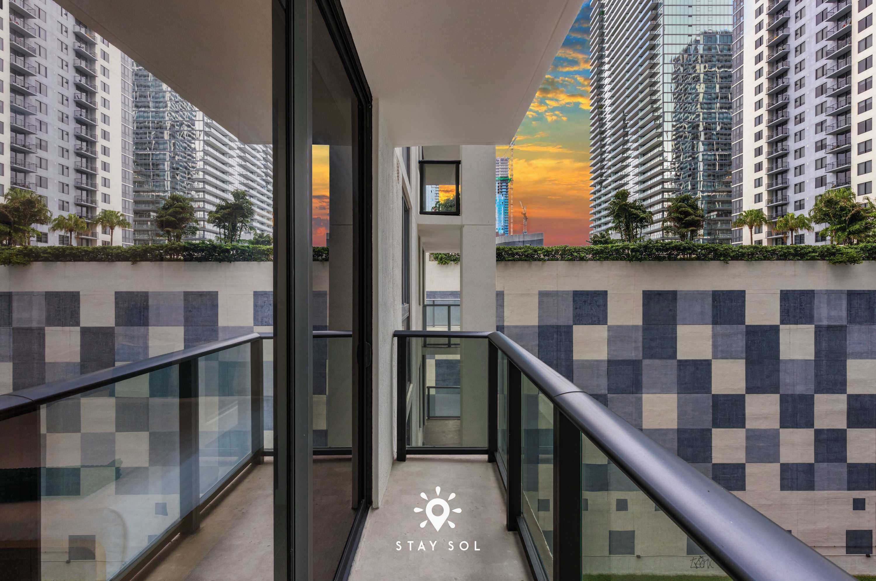 A modern building with a glass balcony, checkered wall pattern, and a view of high-rise buildings.