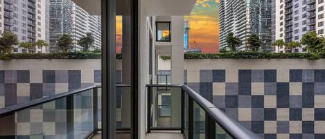 A modern building with a glass balcony, checkered wall pattern, and a view of high-rise buildings.