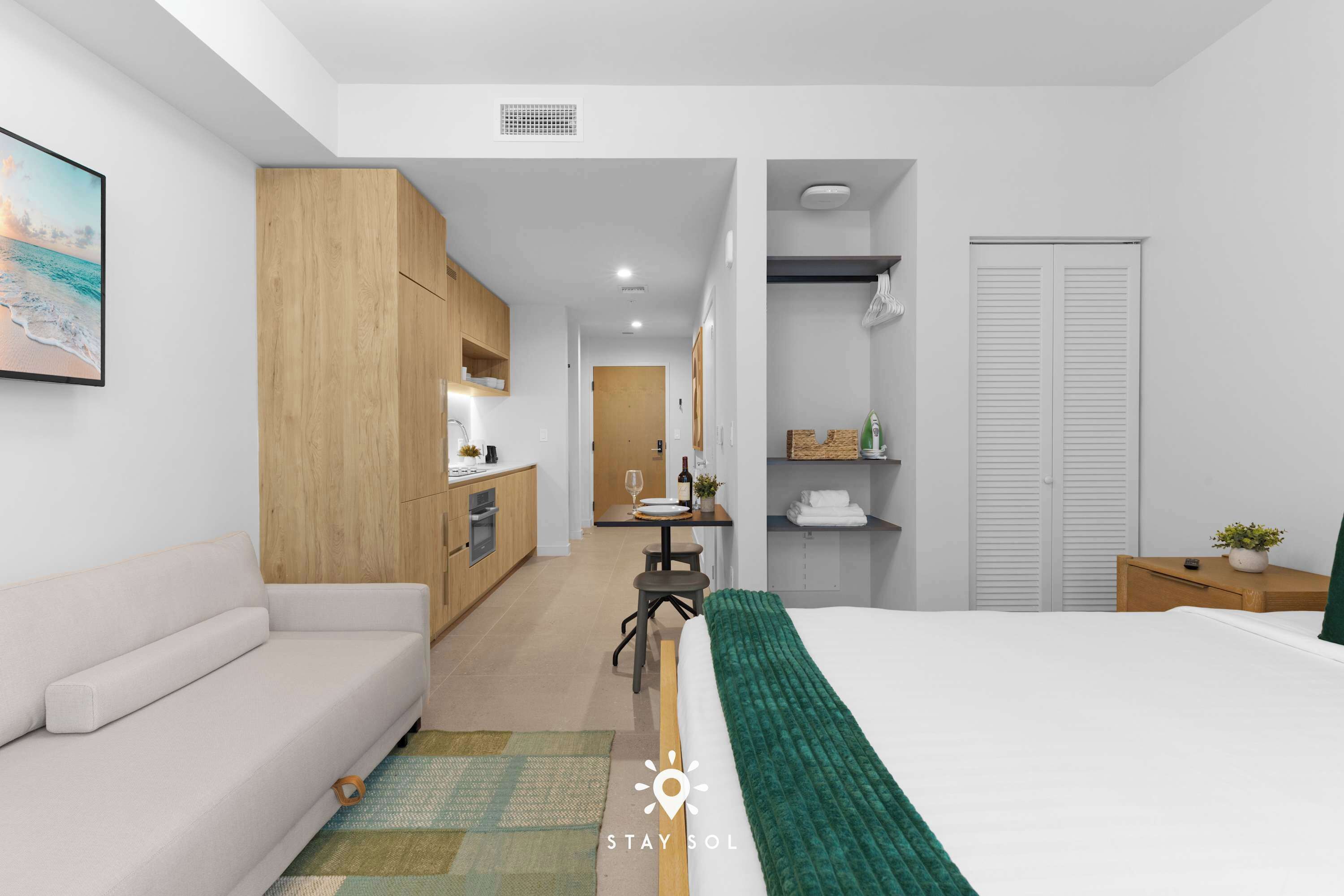 Een moderne hotelkamer met een bed, een bank, een kitchenette en een badkamer.