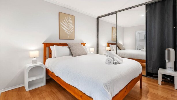 Une chambre d’hôtel moderne avec un grand lit, une table de chevet avec une lampe, un miroir et une œuvre d’art encadrée au mur.