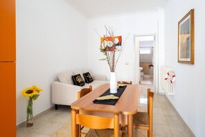 Ein Essbereich mit Holztisch, Stühlen, einer Vase mit Blumen, einer Couch mit Kissen und einem Bild an der Wand.