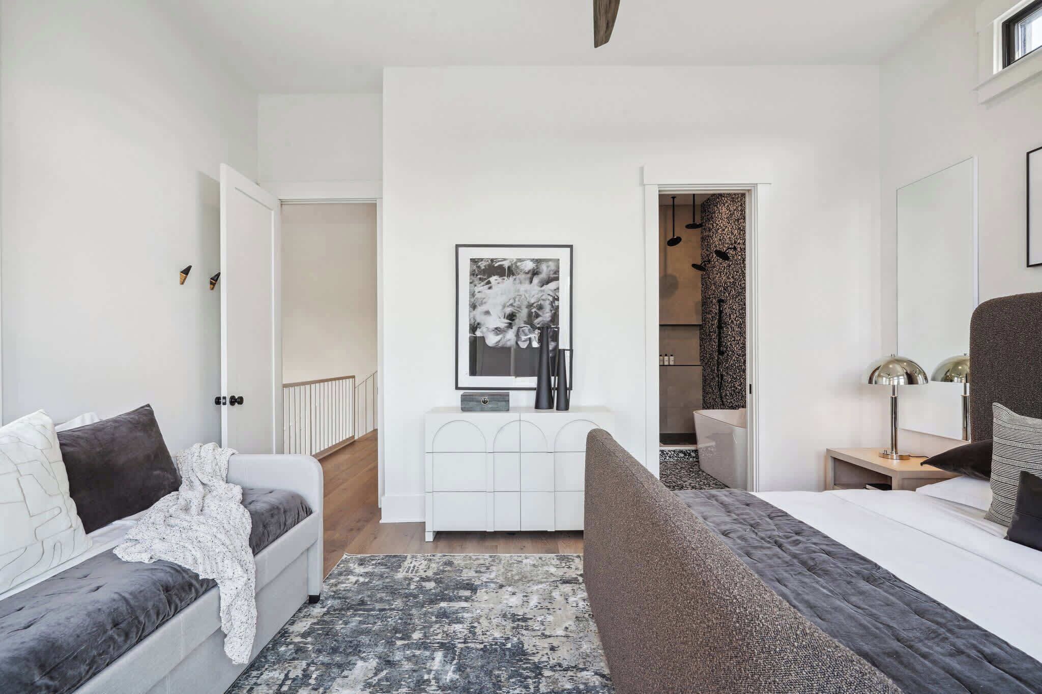 A modern bedroom with a grey sofa, a bed, a white cabinet, and a large mirror.