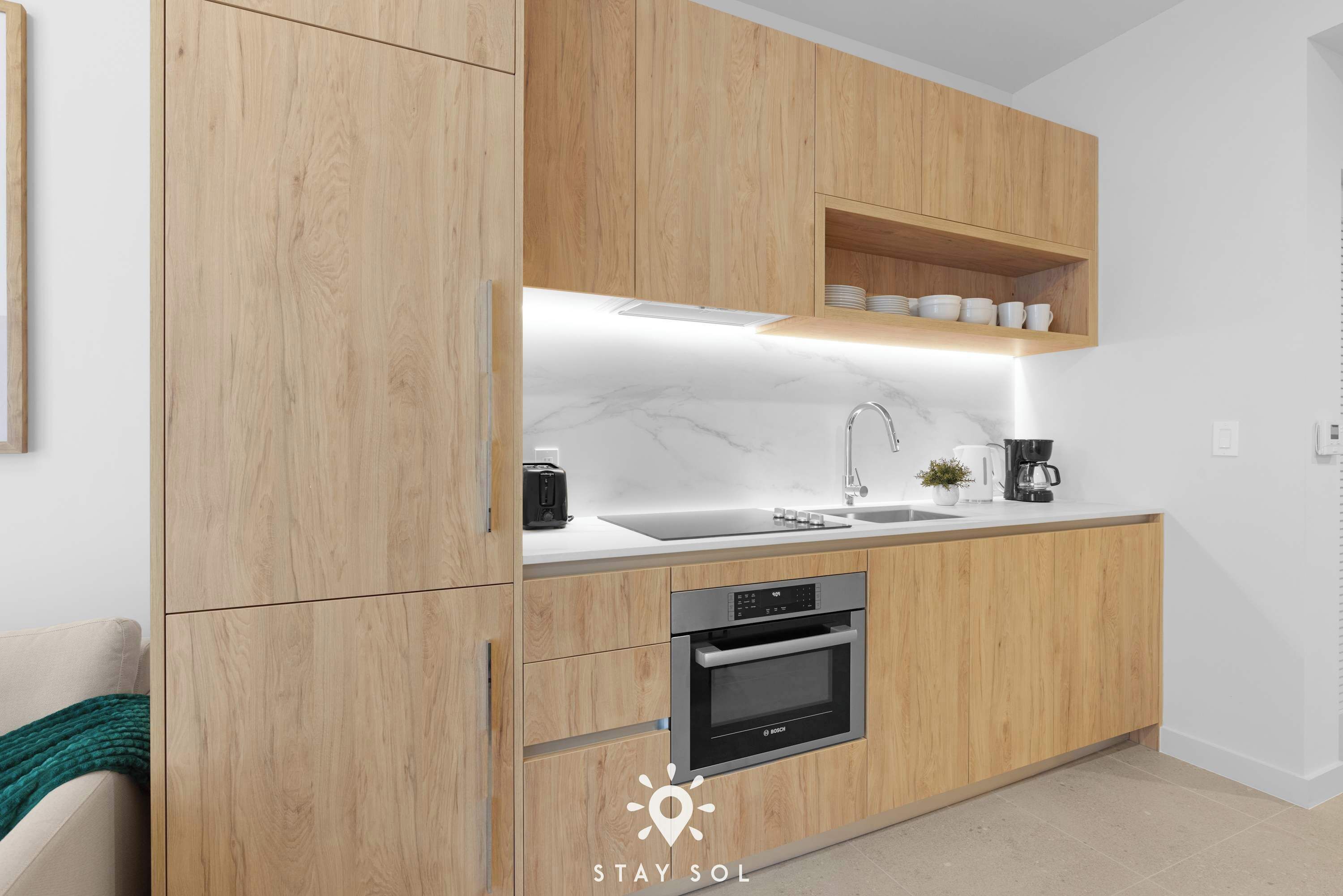 Une cuisine moderne avec des meubles en bois, un four encastré, un évier et une machine à café.
