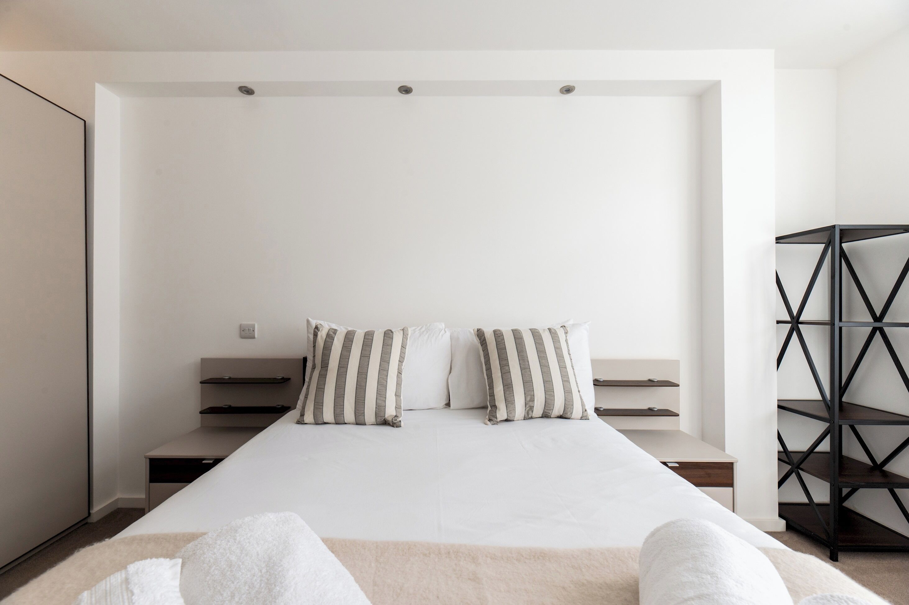 A minimalist bedroom with a large bed, two bedside tables, and a black shelving unit.
