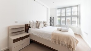 Une chambre à coucher au style minimaliste, avec un lit, des tables de chevet et une fenêtre équipée de stores.
