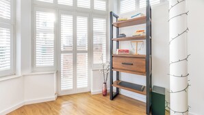Une pièce avec un plancher en bois, une bibliothèque, un vase décoré de branches et un pilier blanc orné de branches.