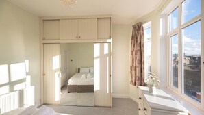 A bedroom with a large mirror, a bed with neatly folded towels, a dresser, and a window with a view of the city. - A beautiful 2-bed mansion-block flat in Putney - Pass the Keys (London)