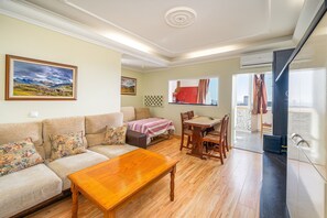 A living room with a sofa, a wooden table, a dining table with chairs, a window with curtains, and an air conditioning unit. - Apartment 'Belmar' with Sea View, Wi-Fi and Air Conditioning (Armação de Pêra)