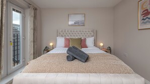 Un lit bien fait, avec une couvre-lit à motifs, une tête de lit capitonnée et deux lampes de chevet.
