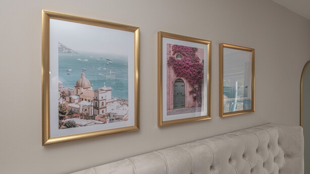 Trois tableaux encadrés sont accrochés au mur, au-dessus d’une tête de lit capitonnée.