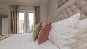 Une chambre à coucher avec un grand lit, une tête de lit capitonnée et une vue sur l’extérieur par une porte.