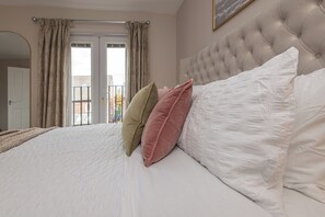A bedroom with a large bed, a tufted headboard, and a view of the outside through a door. - Stylish 5-Bed Townhouse In Wakefield (Crigglestone)