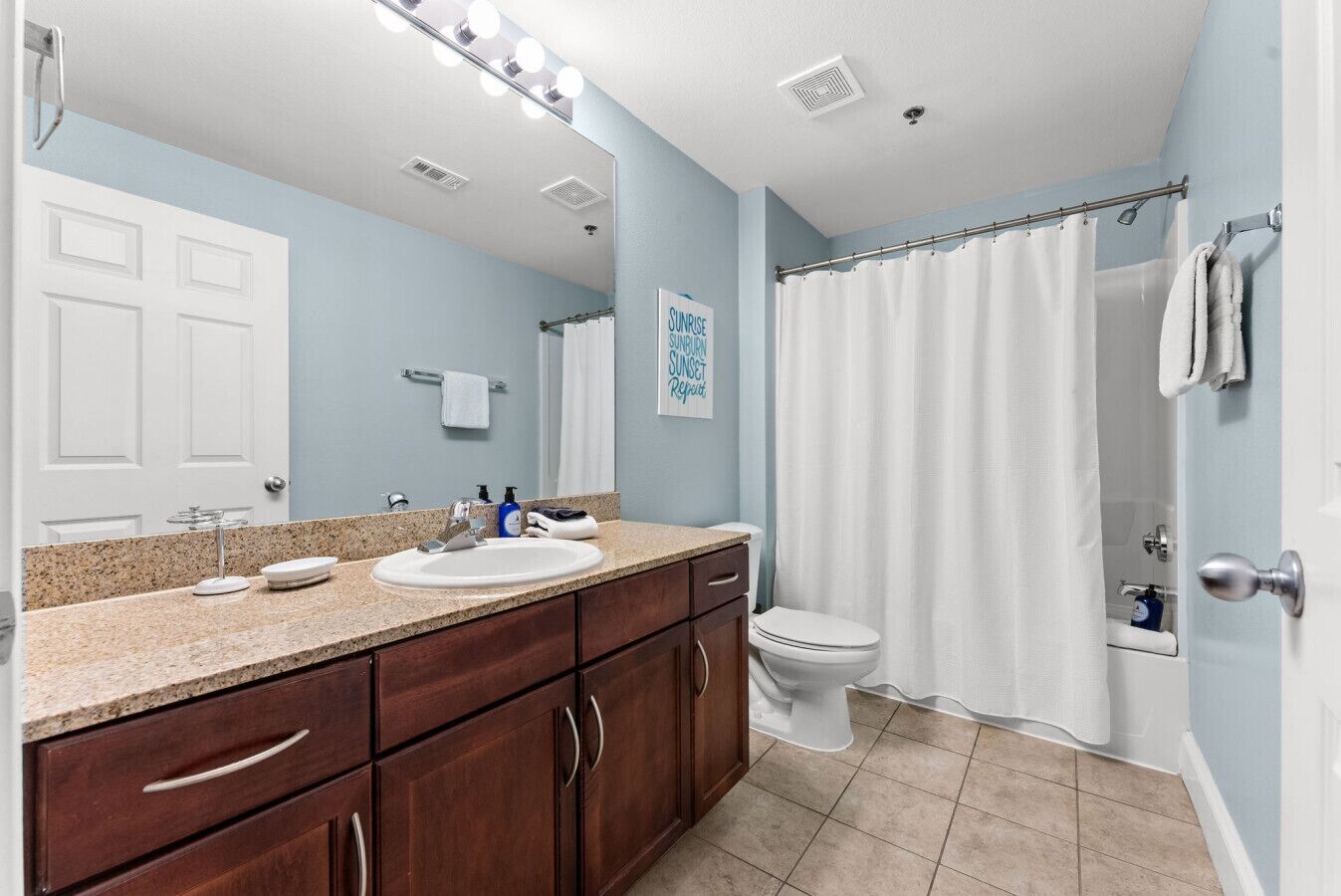 A bathroom with a sink, mirror, and toilet. There is a shower curtain and a towel rack.