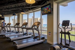 Ein Fitnessstudio mit Laufbändern, einem Ergometer und einem Fernseher, der ein farbenfrohes Bild zeigt.