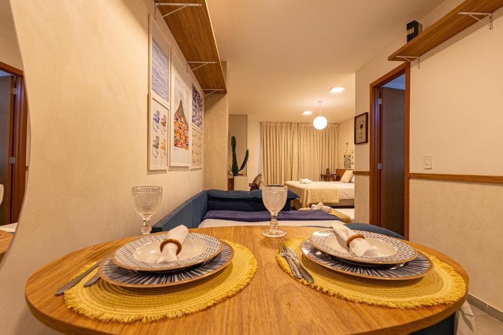 Un coin repas avec deux tables rondes, chacune dressée pour deux personnes, avec assiettes, couverts et un verre. La pièce a une atmosphère chaleureuse, avec un canapé bleu et une petite table en arrière-plan.