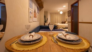 A dining area with two round tables set for two, each with plates, cutlery, and glasses. The room has a modern design with a blue sofa and a large cactus plant in the background. - Cozy apartment in a modern building in the heart of Rio, accommodates up to 6 people. (Rio de Janeiro)