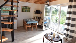 A spacious room with a wooden staircase, a dining area with a table and chairs, a television, and a large sliding glass door leading to an outdoor deck. - House With Private Garden and Sauna (Parchowo)