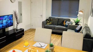 A modern living room with a TV, sofa, dining table, and a window with blinds.
