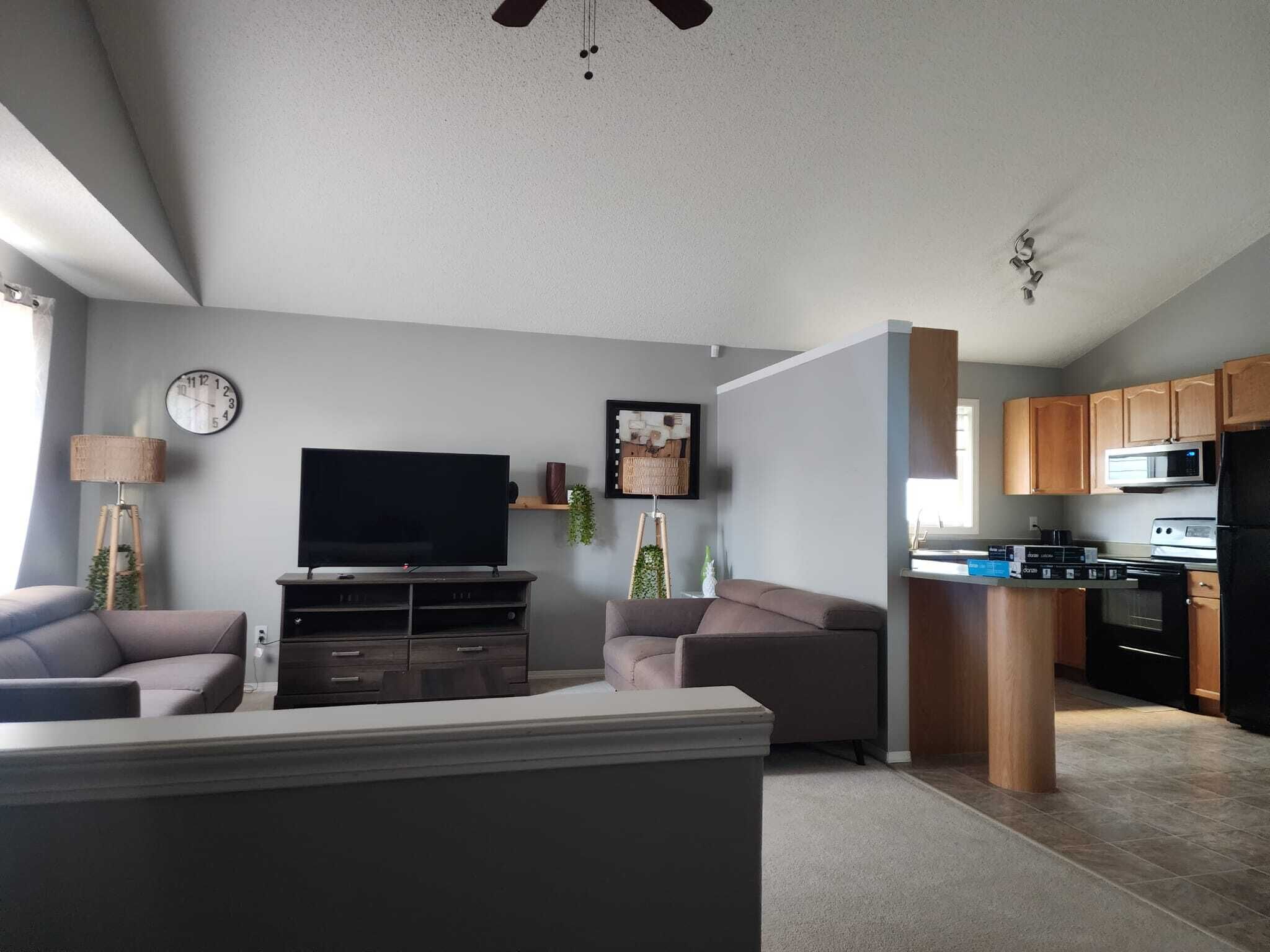 En moderne stue med et fladskærms-tv, sofaer, et sofabord og et spiseområde med et køkken i baggrunden.