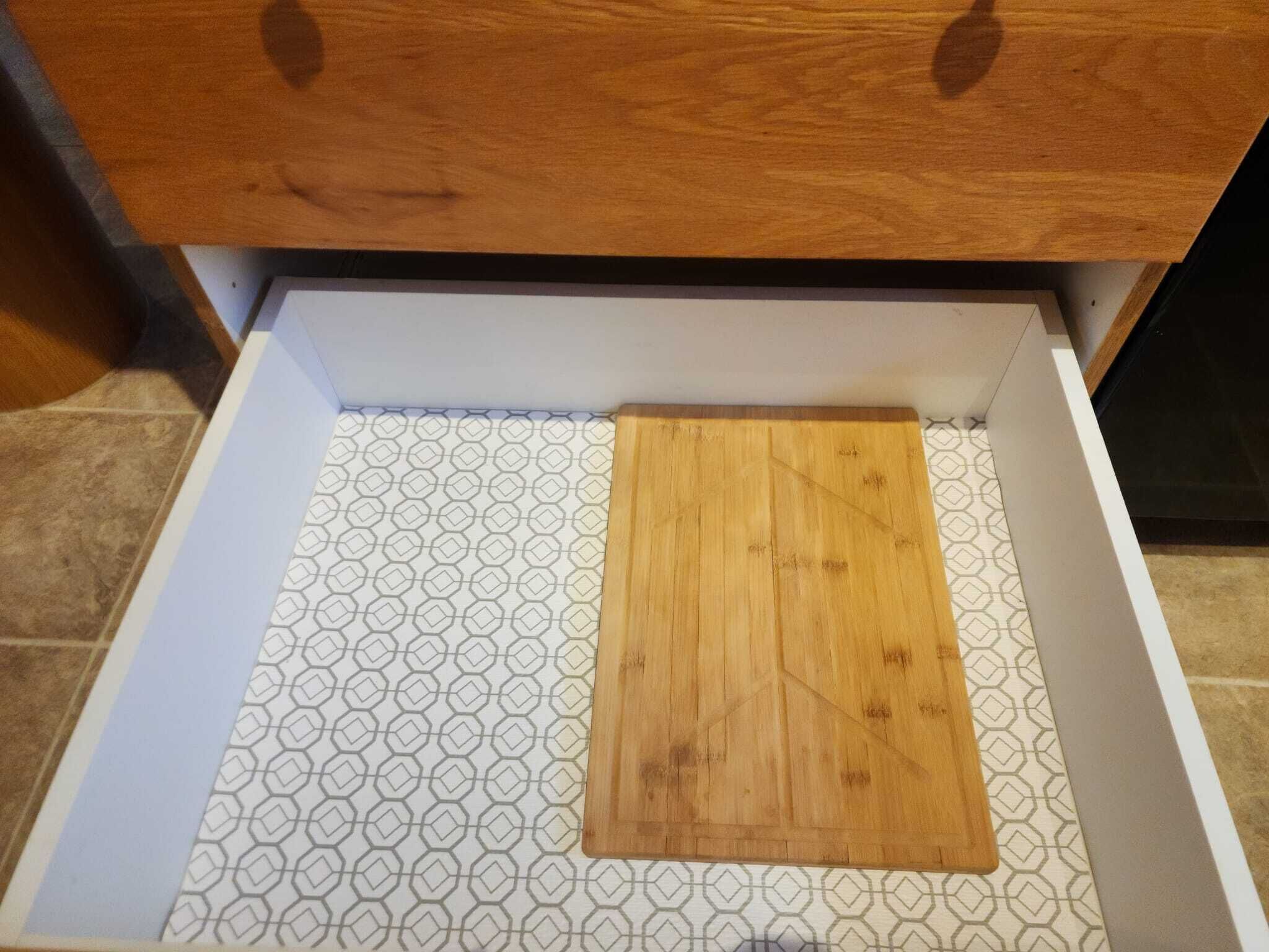 Eine Schublade mit einem geometrisch gemusterten Boden und einem Holzschneidebrett darin.