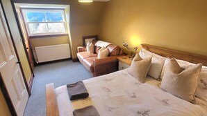 Une chambre d’hôtel avec un lit, un canapé, une table de chevet, une lampe et une fenêtre donnant sur des arbres.