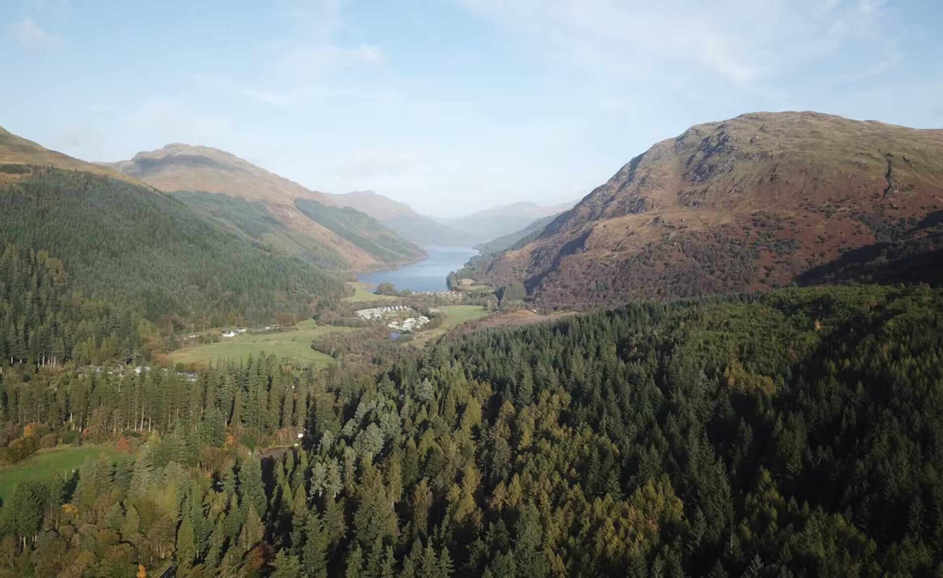 A mountainous landscape with a valley, dense forest, and a body of water.