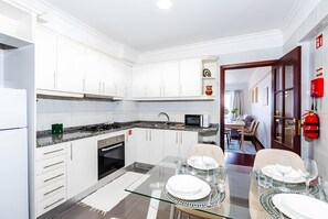 A modern kitchen with white cabinets, a glass dining table set for four, and a view into a dining area.