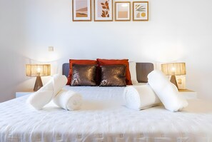 A neatly made bed with white linens and two decorative pillows, a bedside lamp, and a framed picture on the wall.