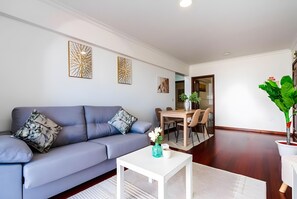 A modern living room with a grey sofa, a white coffee table, and a dining area with a wooden table and chairs.