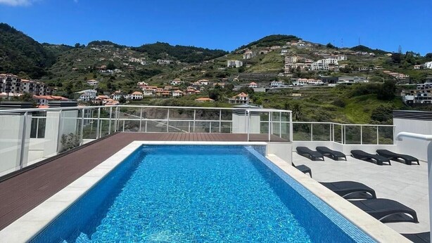 A rooftop pool with a clear view of a hilly landscape in the background. - Casa Sol – Modern Apartment in Central Caniço with Pool and Parking (Caniço)