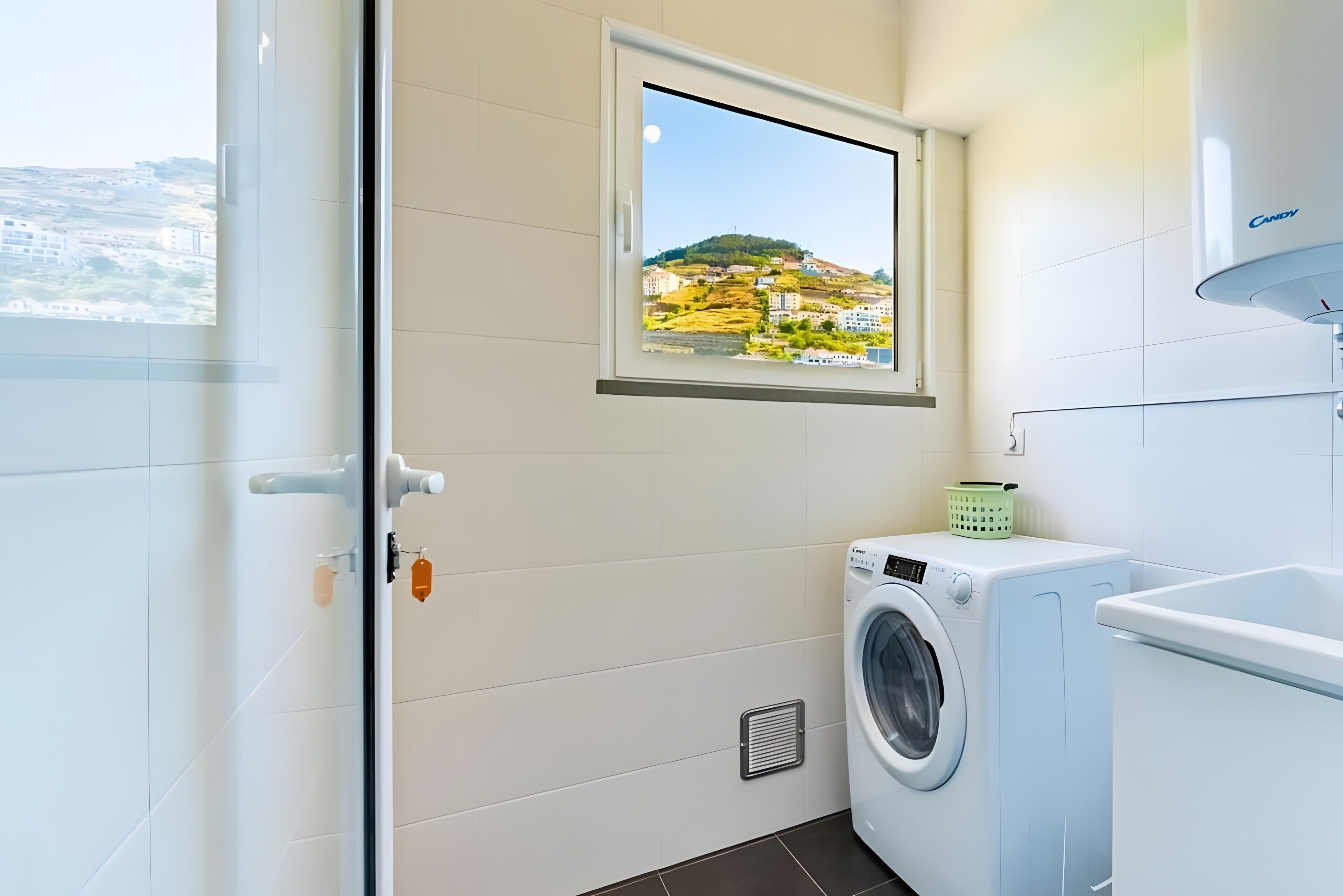 Een wasruimte met een wasmachine, een droger, een raam met uitzicht op een heuvel en een afzuigkap.