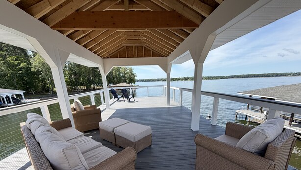 A covered deck with wicker furniture and a view of a lake.