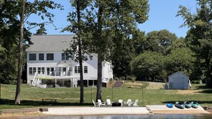 A two-story house with a balcony, a dock with chairs and kayaks, and a small shed.