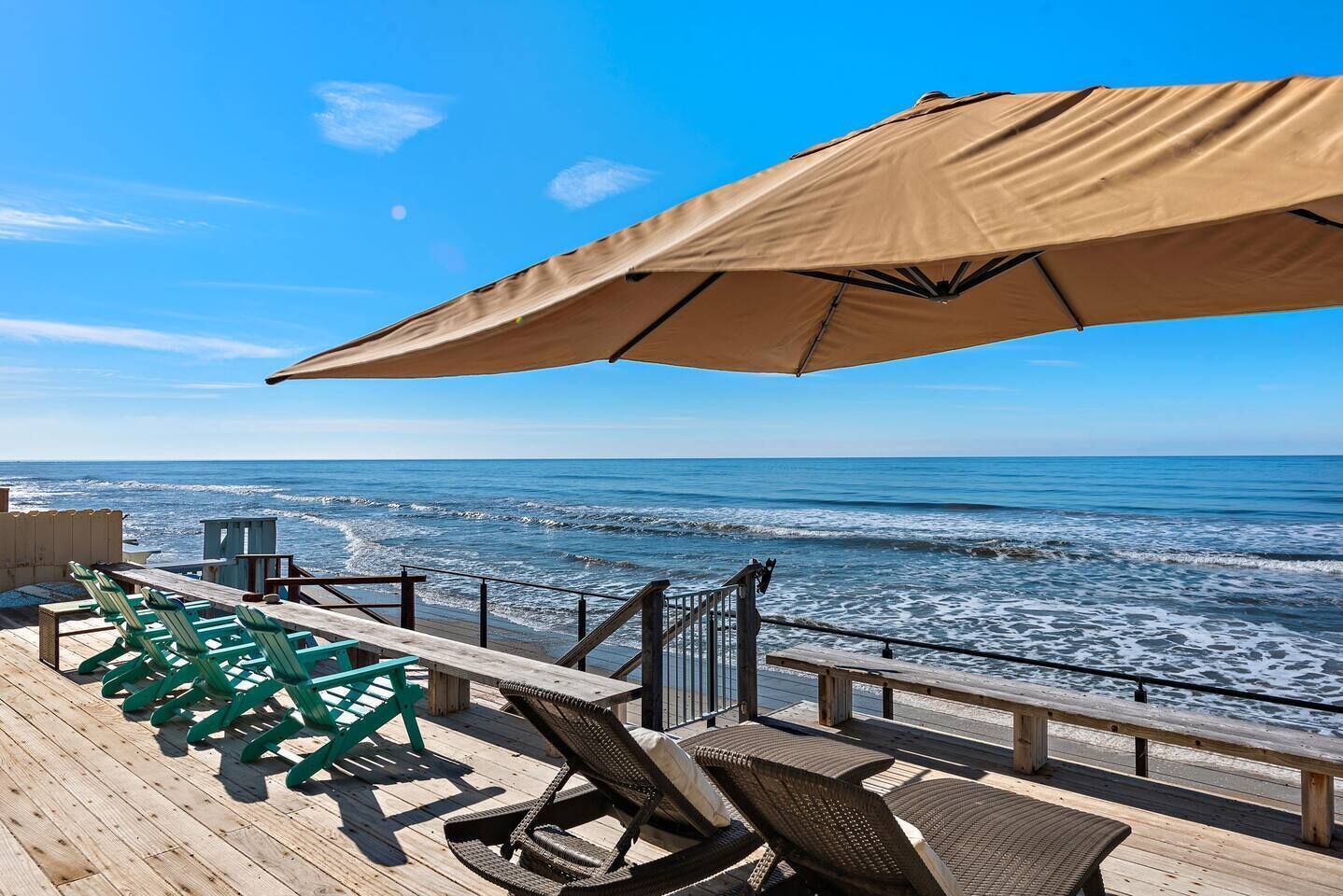 A wooden deck with outdoor seating and a large umbrella overlooking the ocean.