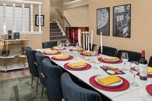 A dining area with a long table set for a meal, featuring red and white tableware, gold accents, and a bottle of wine. - The Backyard Movie, Hot Tub & 2 Game Rooms (Arvada)