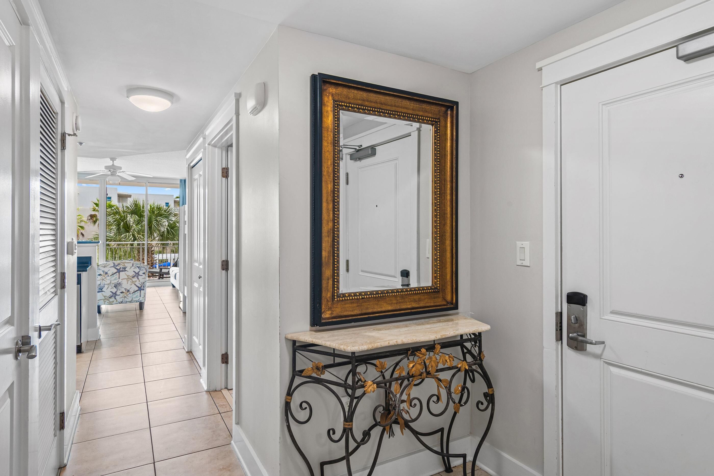 A hallway with a white door, a large mirror with a gold frame, and a black metal console table.
