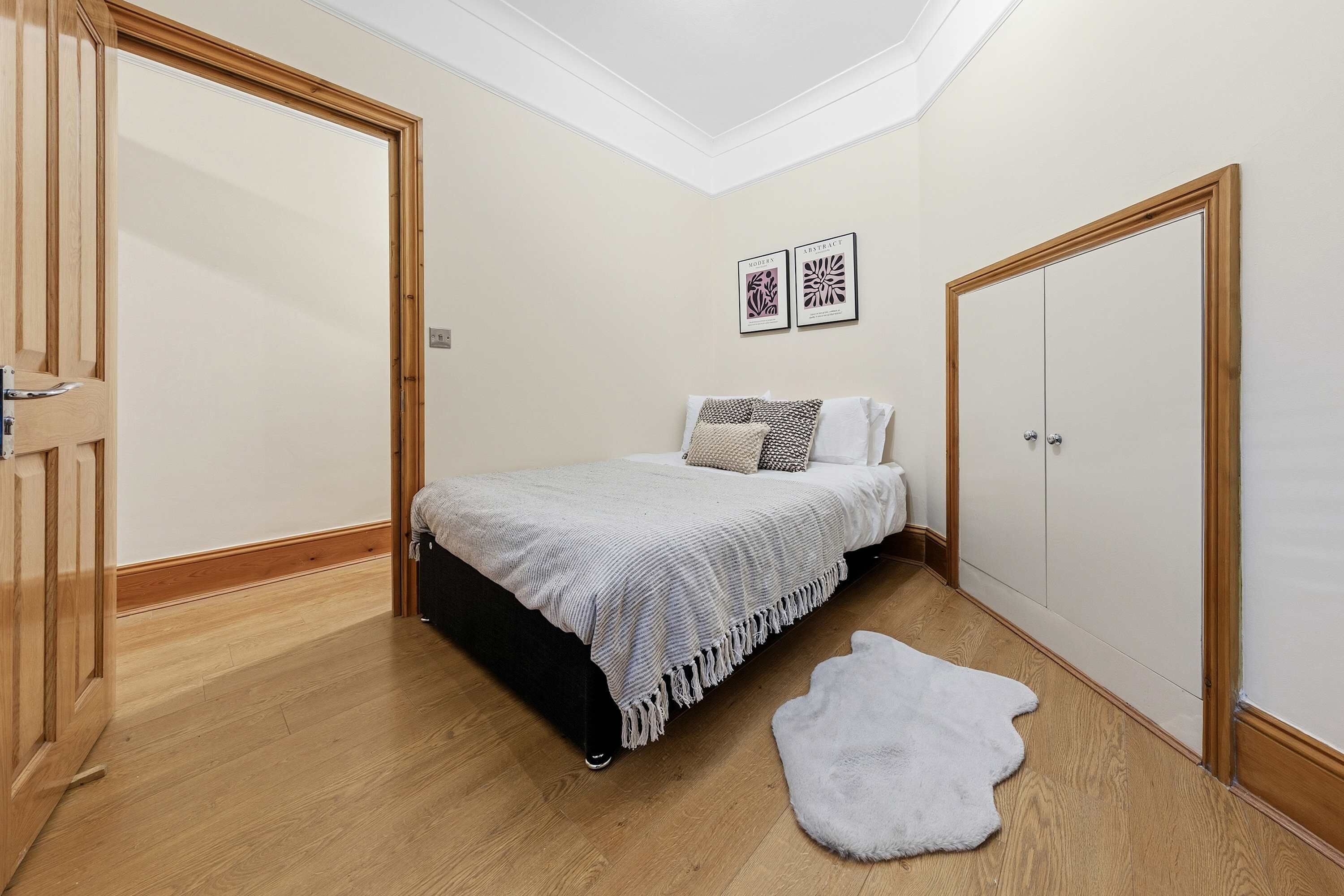 Ein Schlafzimmer mit einem Bett, einem weißen, flauschigen Teppich, einem Kleiderschrank und zwei gerahmten Bildern an der Wand.