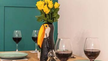 Une table à manger sur laquelle se trouve un grand vase en forme d’oiseau, rempli de fleurs jaunes, et qui est entourée de verres à vin et d’assiettes.