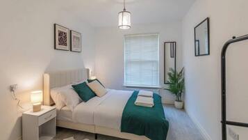 A modern bedroom with a bed, bedside lamp, window with blinds, and a potted plant.